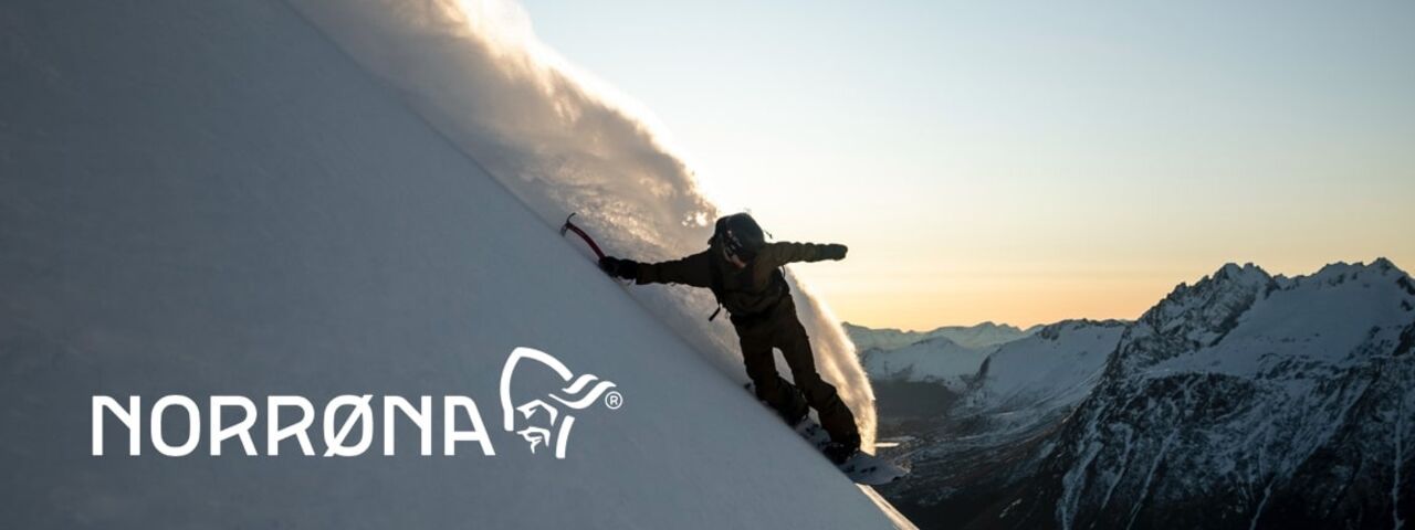 Powder-Ride bei Sonnenuntergang: Wintersportler surft steile Schneehänge in NORRØNA-Gear – perfekte Ausrüstung für extreme Bedingungen.