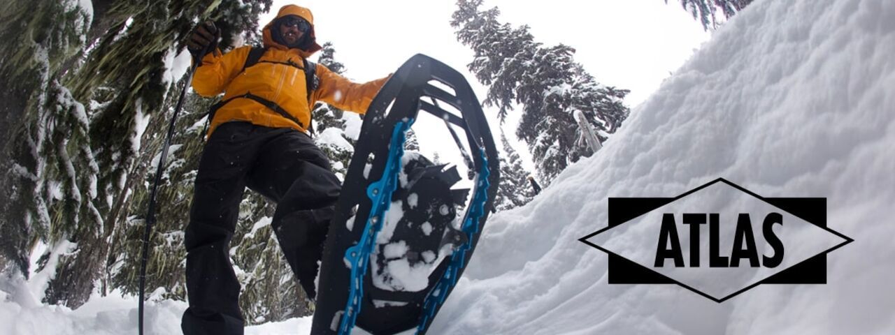 Schneeschuhwanderer mit orangefarbener Jacke und moderner Ausrüstung in tief verschneitem Winterwald – Blick auf Atlas-Schneeschuhe im Einsatz.