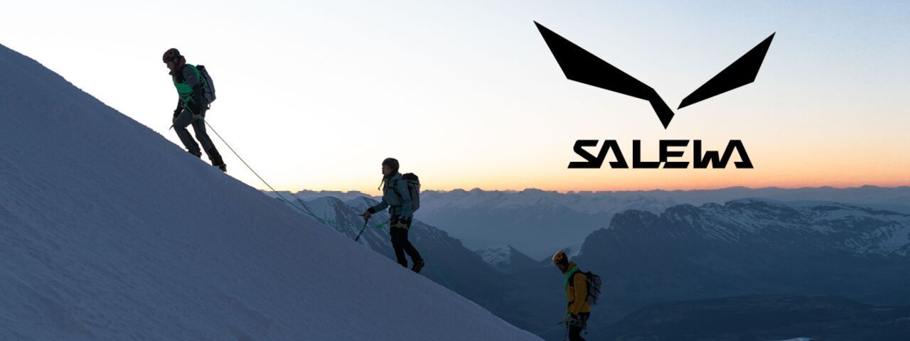 Drei Bergsteiger mit Salewa-Ausrüstung beim Aufstieg im Schnee bei Sonnenaufgang – Alpinismus in den Dolomiten.