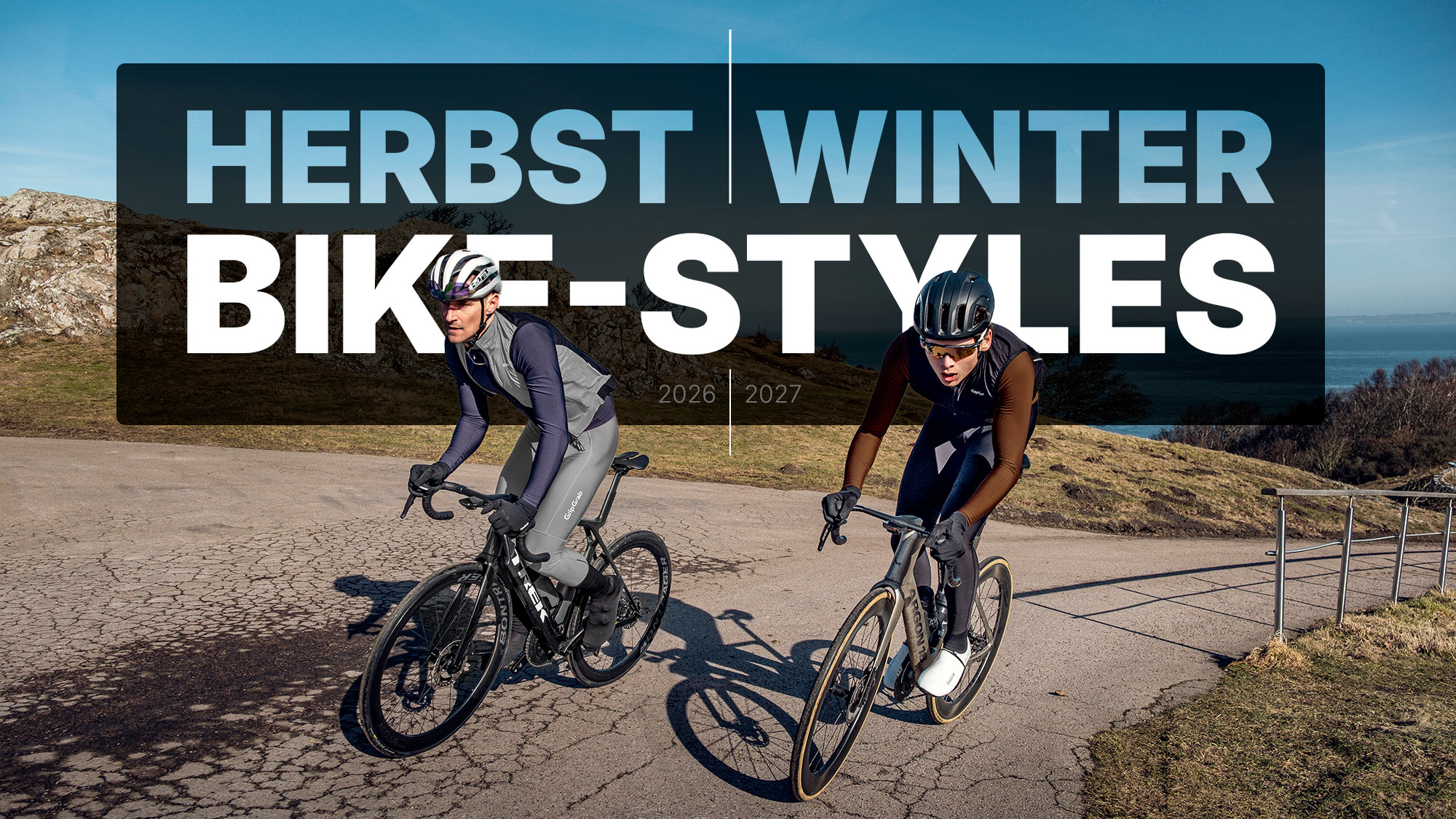 Zwei Rennradfahrer in sportlicher Herbst-Winter-Bekleidung auf einer Küstenstraße, Bike-Styles 2026/27
